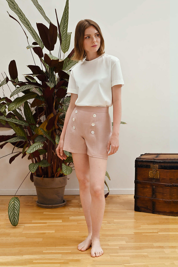 This old pink high-waisted short. There is a row of white river shell buttons on each side of the leg. 